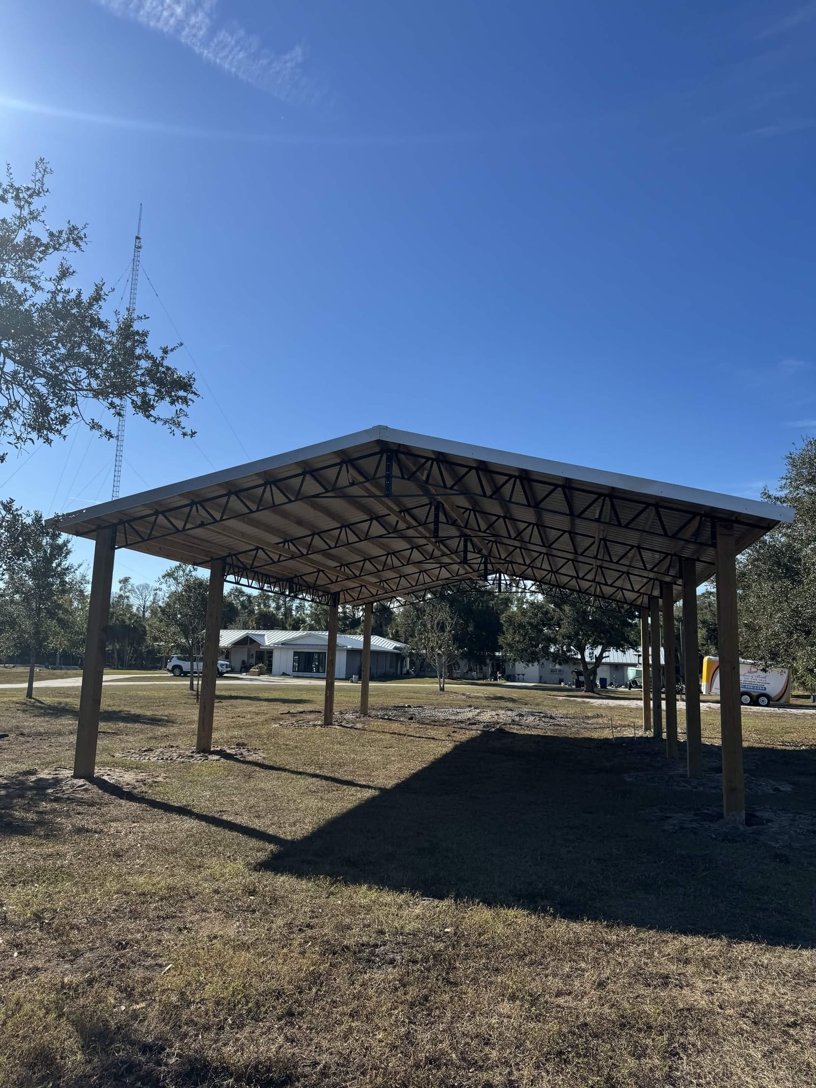 Completed open-sided pole barn cover with steel trusses on a clear blue-sky day
