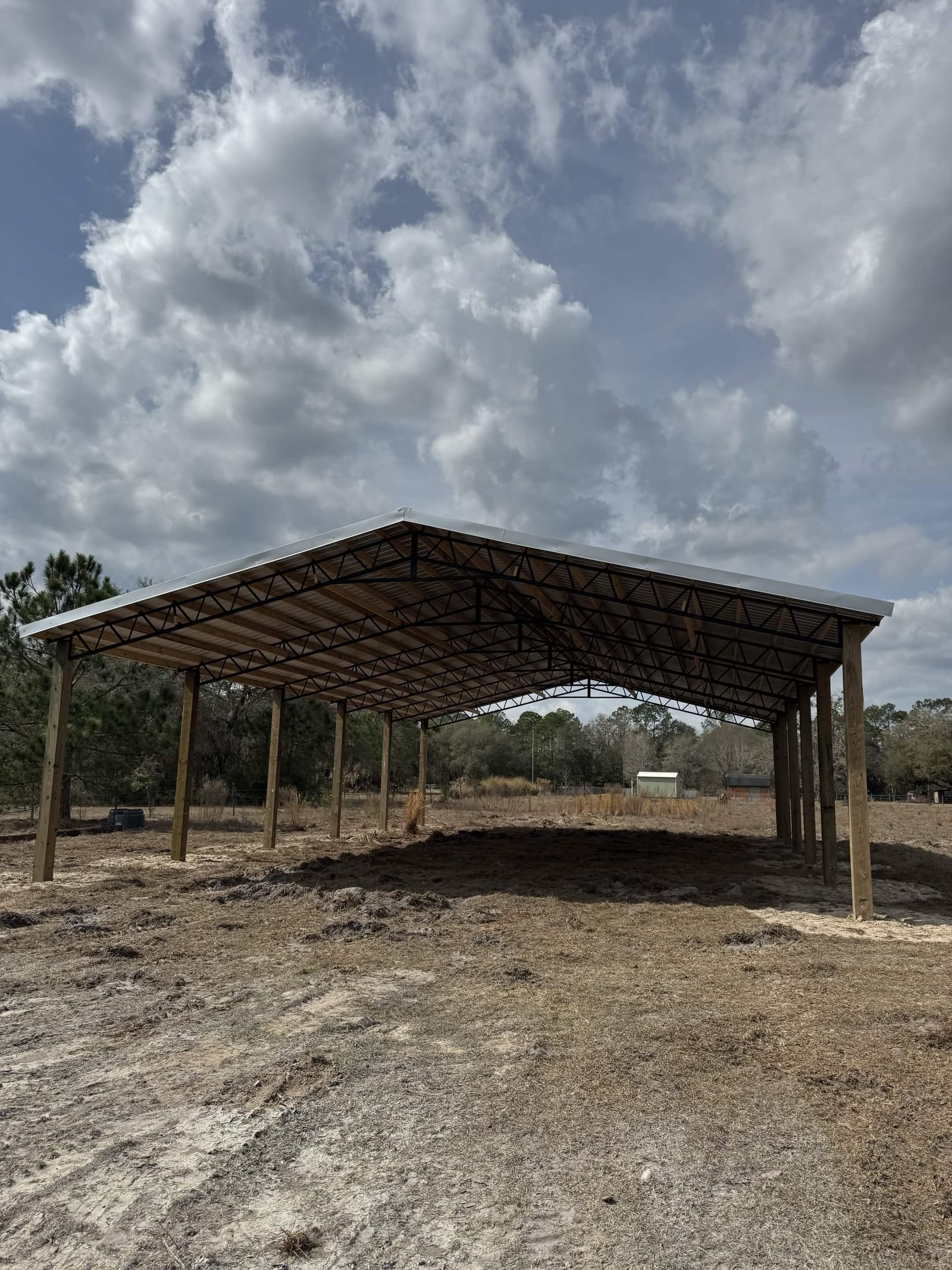 Large open-sided pole barn with treated posts under dramatic cumulus clouds